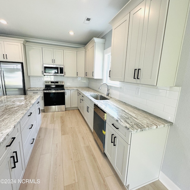 kitchen with tasteful backsplash, light stone counters, light hardwood / wood-style floors, appliances with stainless steel finishes, and sink