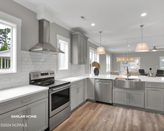 kitchen with stainless steel appliances, light countertops, hanging light fixtures, visible vents, and wall chimney exhaust hood