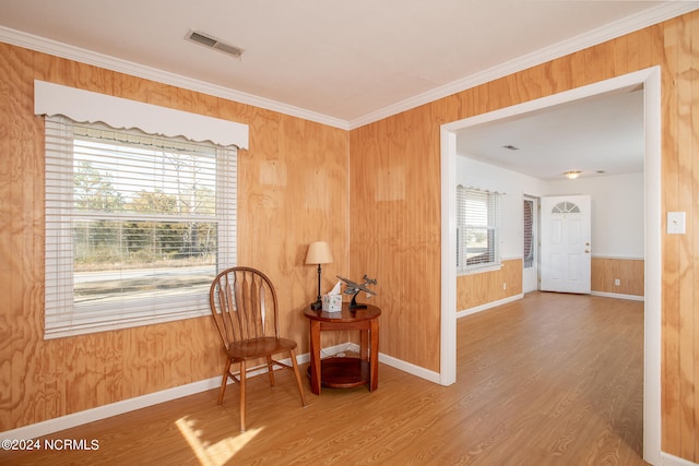 living area featuring wood walls, ornamental molding, and light wood-type flooring