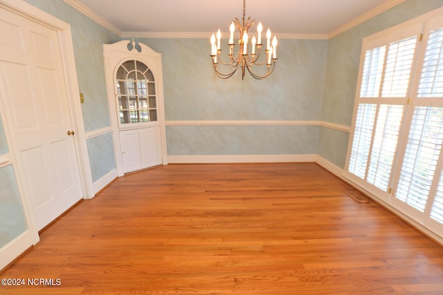 unfurnished dining area featuring a wealth of natural light, crown molding, light wood-type flooring, and an inviting chandelier