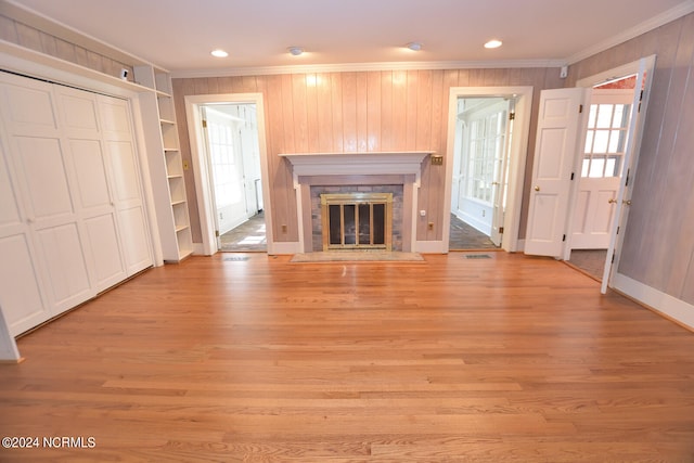 unfurnished living room featuring wood walls, ornamental molding, and light wood-type flooring