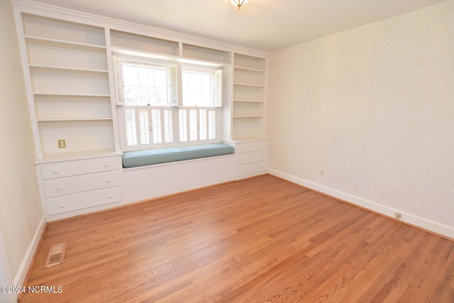 empty room with built in shelves and light hardwood / wood-style flooring