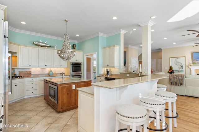 kitchen featuring decorative light fixtures, light stone counters, stainless steel appliances, a kitchen island with sink, and ceiling fan with notable chandelier