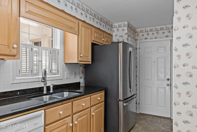 kitchen with sink, white dishwasher, a textured ceiling, dark tile flooring, and stainless steel refrigerator