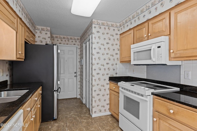 kitchen with white appliances, dark tile floors, a textured ceiling, and dark stone counters