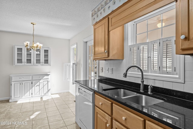 kitchen featuring white dishwasher, pendant lighting, a notable chandelier, dark stone counters, and sink