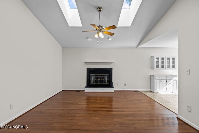 unfurnished living room with vaulted ceiling with skylight, ceiling fan, and dark tile flooring