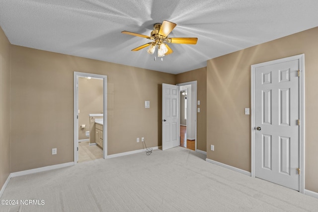 unfurnished bedroom featuring light carpet, ensuite bath, ceiling fan, and a textured ceiling