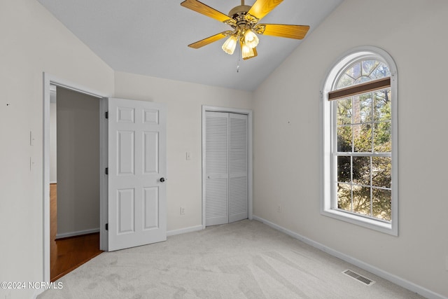 unfurnished bedroom featuring ceiling fan, multiple windows, light colored carpet, and vaulted ceiling