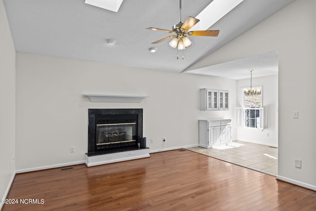 unfurnished living room featuring light tile flooring, vaulted ceiling with skylight, and ceiling fan with notable chandelier