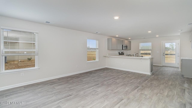 kitchen with kitchen peninsula, plenty of natural light, stainless steel appliances, and light hardwood / wood-style flooring