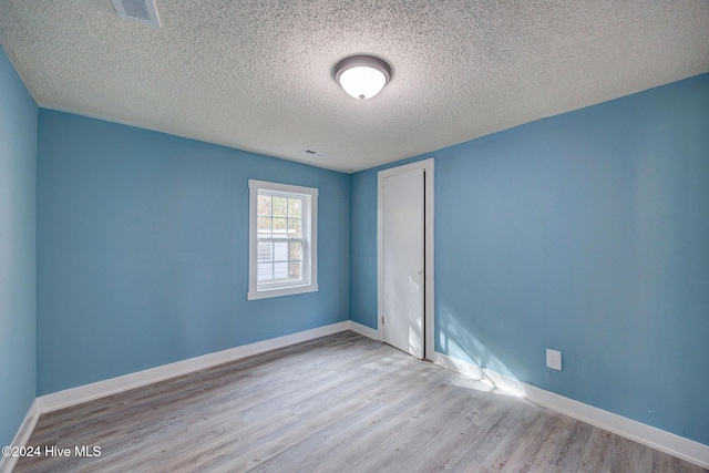 empty room with a textured ceiling and light hardwood / wood-style floors