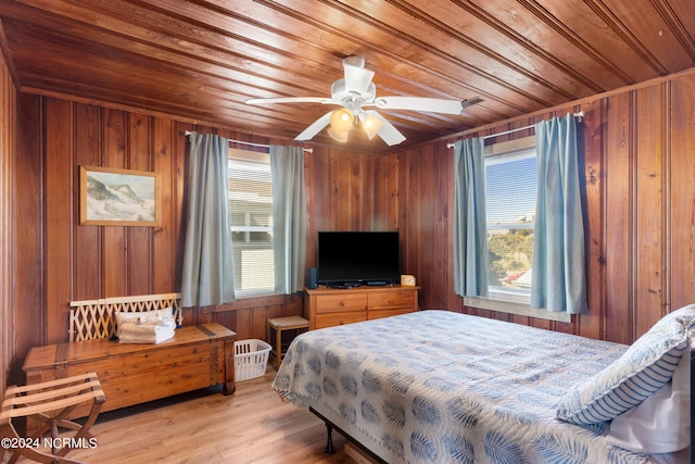 bedroom with wooden walls, light wood-type flooring, and multiple windows