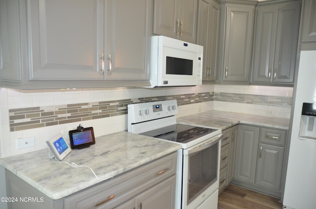 kitchen featuring gray cabinetry, white appliances, light stone counters, wood-type flooring, and tasteful backsplash