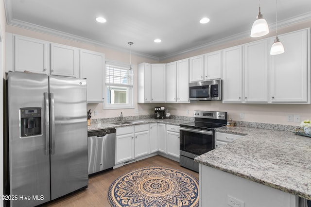 kitchen with white cabinets, a sink, stainless steel appliances, decorative light fixtures, and wood finished floors