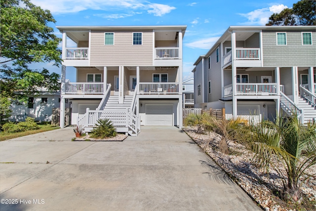 raised beach house with a garage, covered porch, a balcony, concrete driveway, and stairway