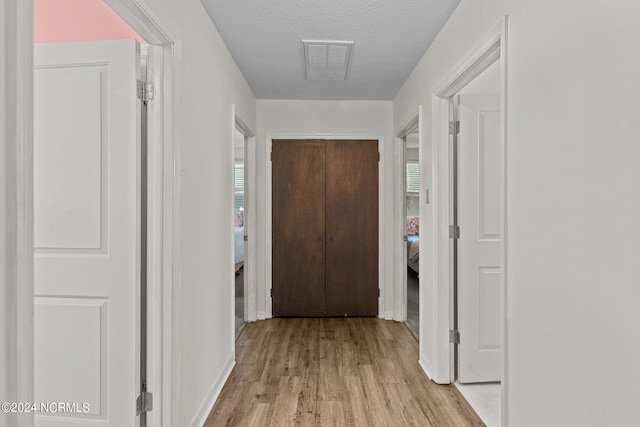 hall with a textured ceiling and light hardwood / wood-style floors