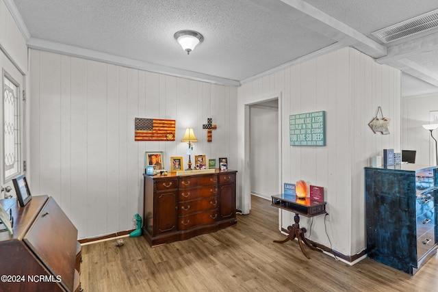 interior space featuring wood walls, beam ceiling, a textured ceiling, and light wood-type flooring