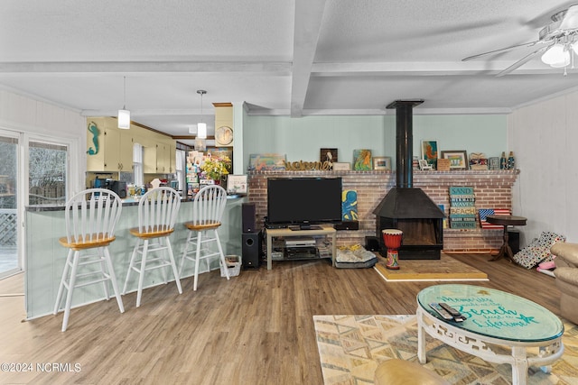 living room with beam ceiling, wood-type flooring, ceiling fan, and a wood stove