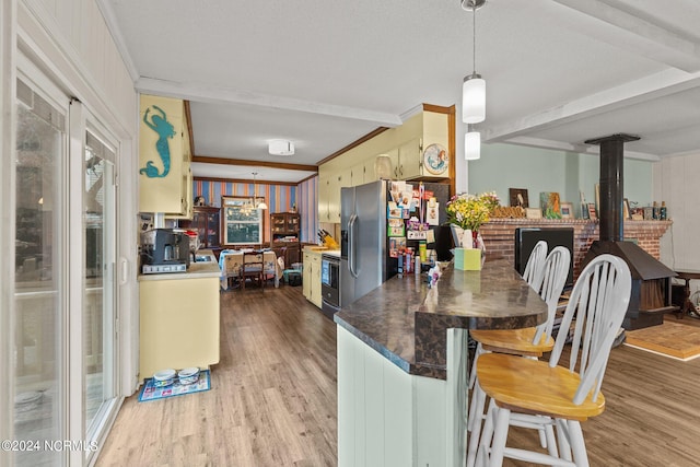 kitchen with stainless steel fridge, a wood stove, beam ceiling, and hardwood / wood-style floors