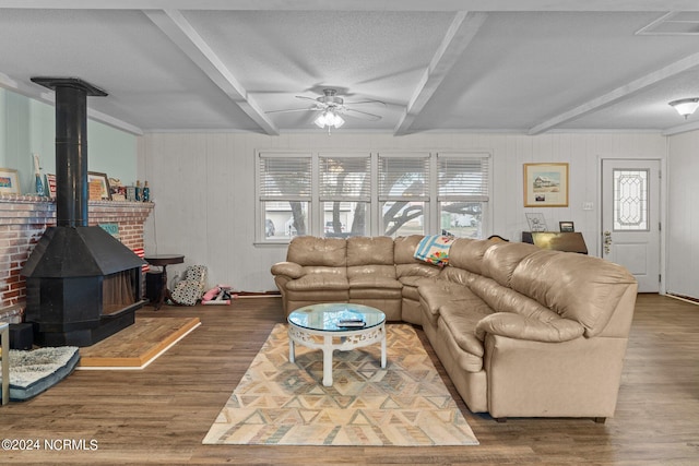 living room with wood-type flooring, ceiling fan, a wood stove, and beamed ceiling