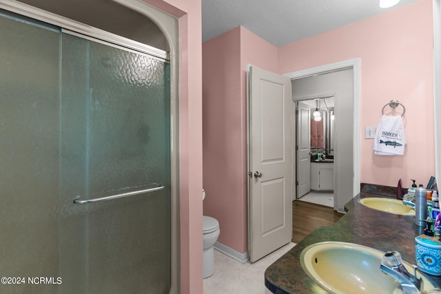 bathroom featuring tile floors, a shower with door, a textured ceiling, toilet, and double vanity