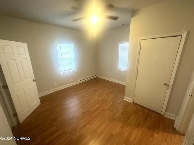 additional living space with a baseboard heating unit, a wealth of natural light, ceiling fan, and dark hardwood / wood-style flooring