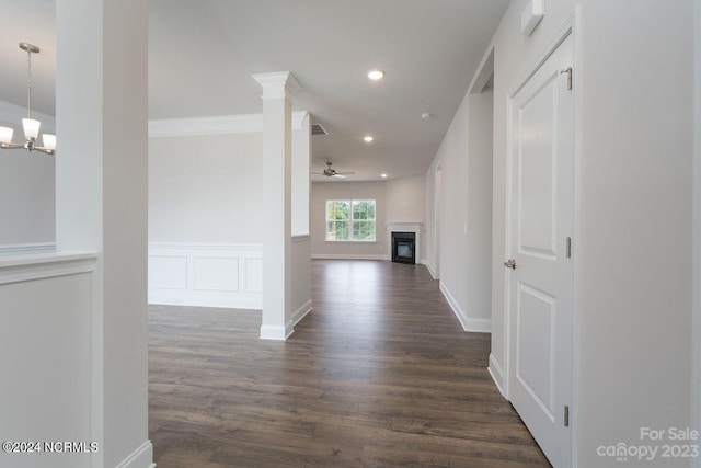 corridor with ornate columns, crown molding, dark wood-type flooring, and an inviting chandelier