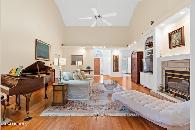 living room featuring light wood-type flooring, a fireplace, ceiling fan, and high vaulted ceiling