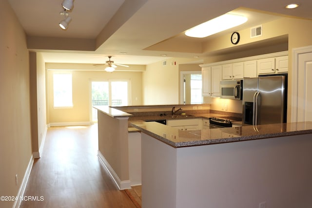 kitchen with dark stone countertops, kitchen peninsula, sink, stainless steel appliances, and white cabinets