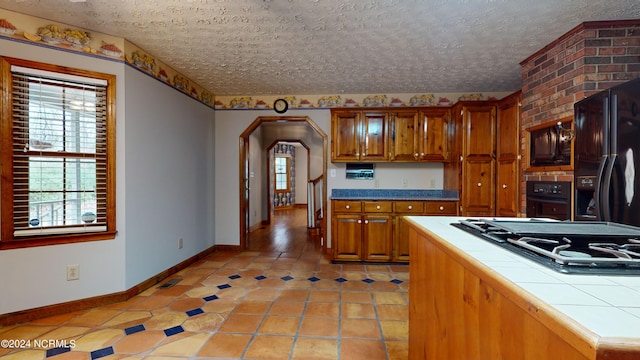 kitchen with light tile floors, brick wall, a textured ceiling, black appliances, and tile counters