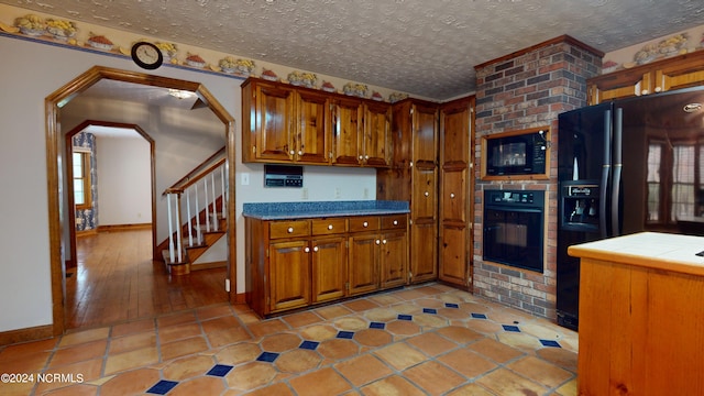 kitchen with brick wall, light tile floors, tile countertops, black appliances, and a textured ceiling