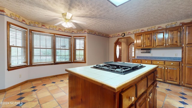 kitchen with ceiling fan, light tile floors, gas stovetop, tile countertops, and a center island