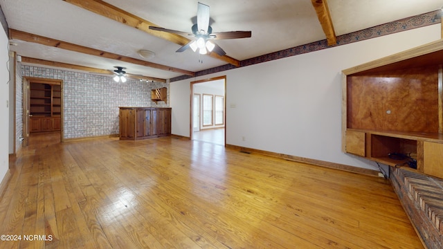 unfurnished living room featuring beamed ceiling, brick wall, ceiling fan, and light wood-type flooring