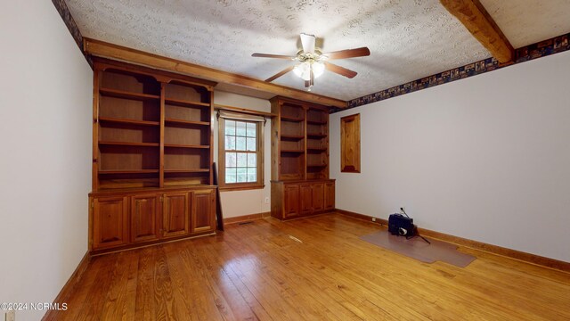 spare room featuring light hardwood / wood-style floors, a textured ceiling, ceiling fan, and beamed ceiling