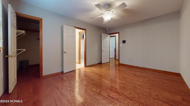 unfurnished bedroom featuring ceiling fan, a walk in closet, dark hardwood / wood-style floors, and a closet