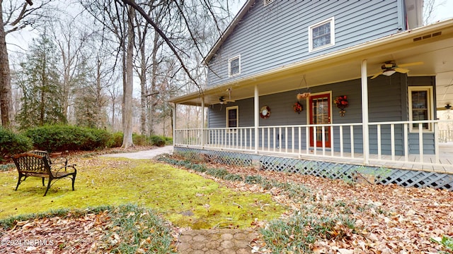 view of side of property with ceiling fan, a lawn, and covered porch