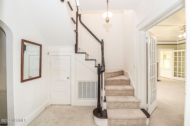 stairs featuring light carpet, ornamental molding, and ceiling fan