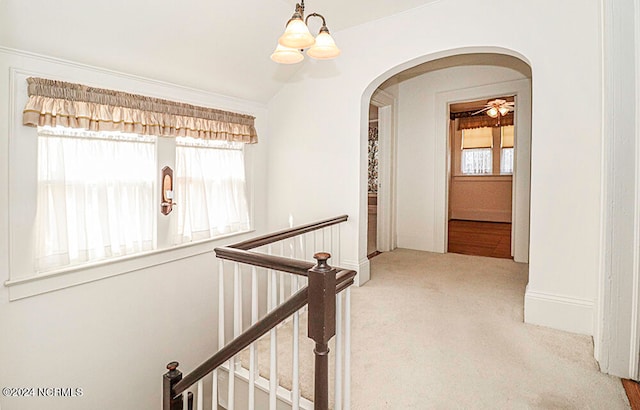 corridor featuring light colored carpet, a healthy amount of sunlight, and a chandelier