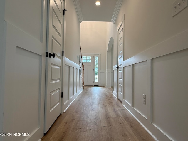 corridor with ornamental molding, a high ceiling, and light hardwood / wood-style flooring