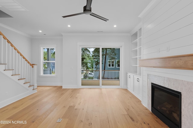 unfurnished living room featuring light hardwood / wood-style flooring, ceiling fan, built in features, ornamental molding, and a tiled fireplace