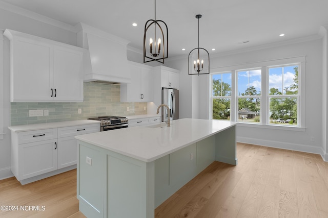 kitchen with white cabinetry, hanging light fixtures, stainless steel appliances, premium range hood, and an island with sink