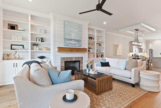 living room featuring light hardwood / wood-style floors, ornamental molding, a fireplace, ceiling fan with notable chandelier, and built in shelves