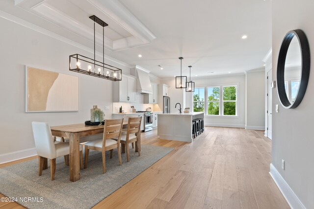 dining area featuring sink, a chandelier, light hardwood / wood-style floors, and a tray ceiling