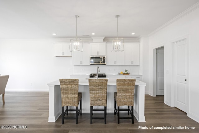 kitchen featuring a breakfast bar area, a kitchen island with sink, white cabinets, light countertops, and stainless steel microwave