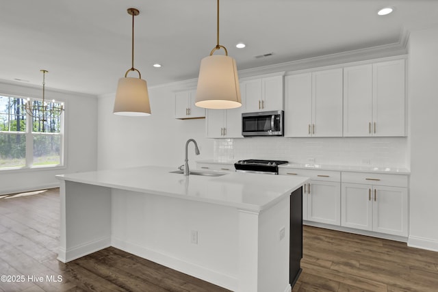 kitchen with a center island with sink, white cabinets, tasteful backsplash, a sink, and appliances with stainless steel finishes