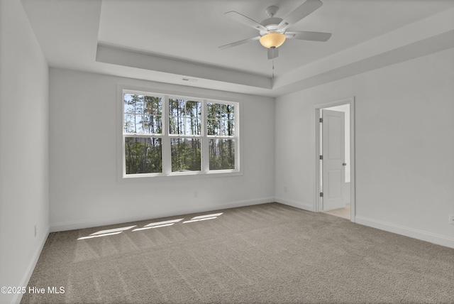 empty room with baseboards, carpet flooring, ceiling fan, and a tray ceiling