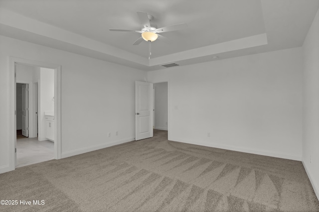 unfurnished bedroom featuring visible vents, ensuite bathroom, baseboards, a raised ceiling, and carpet