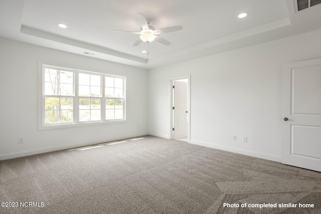 empty room with a tray ceiling, baseboards, carpet, and recessed lighting