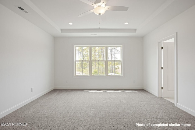 carpeted spare room featuring a tray ceiling, visible vents, baseboards, and recessed lighting